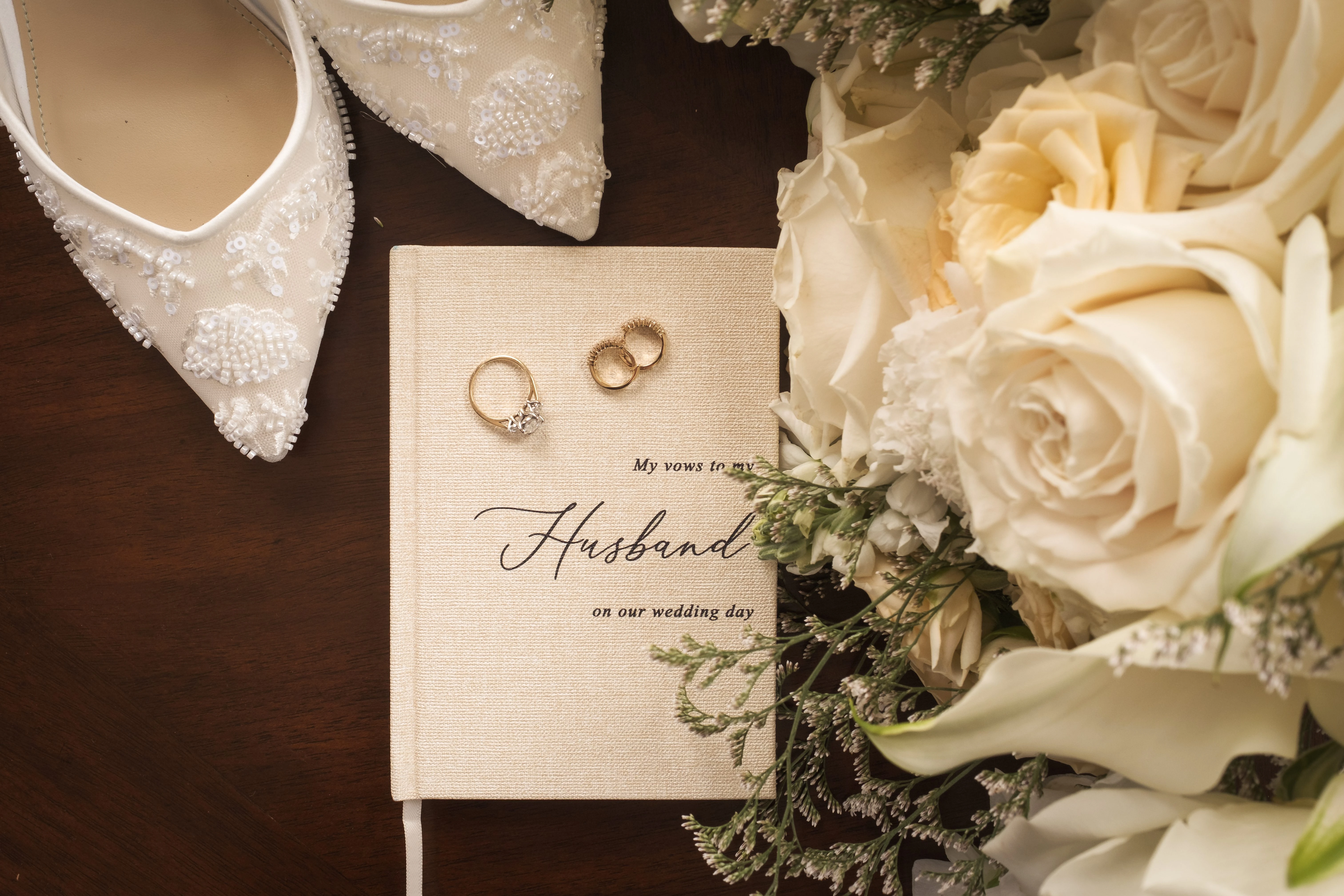 Wedding rings rest beside a rose bouquet and the bride’s shoes