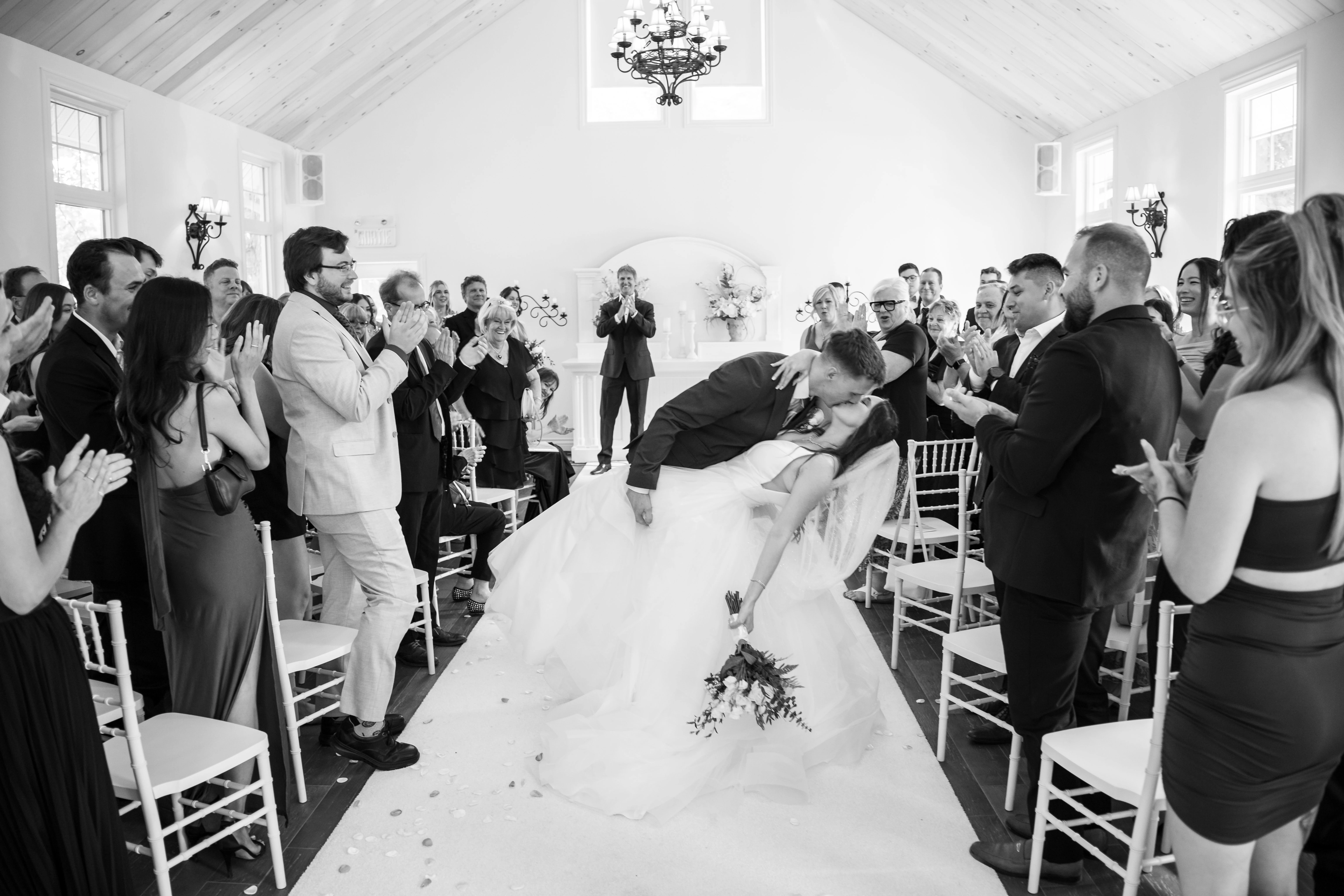 The newlyweds kiss among cheering guests in black and white