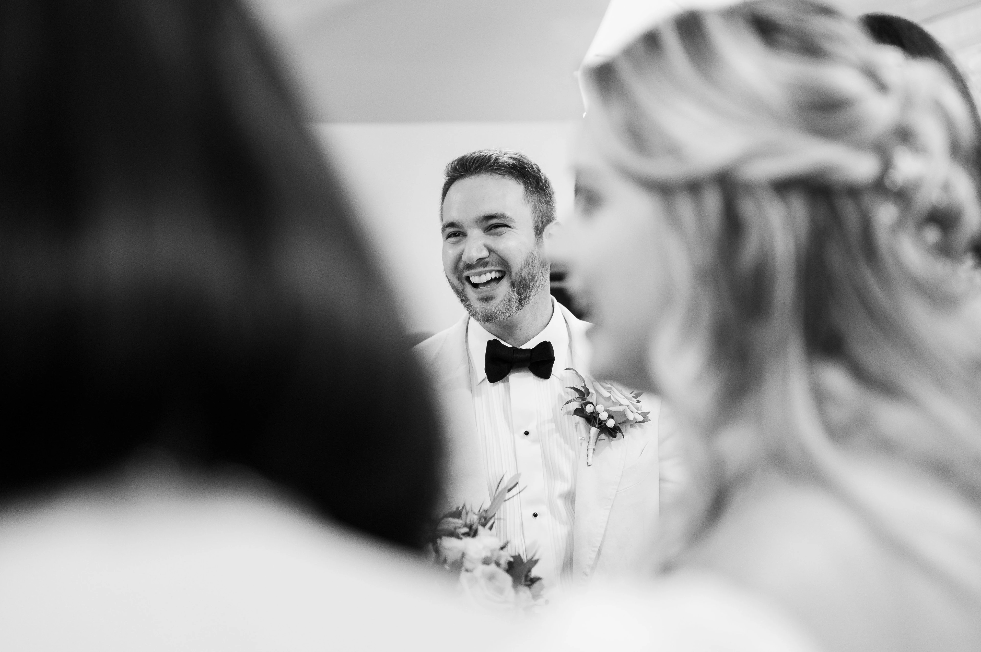 A bride sits on a bench fastening her sandals, with a bouquet of roses and white anemones resting on the bed
