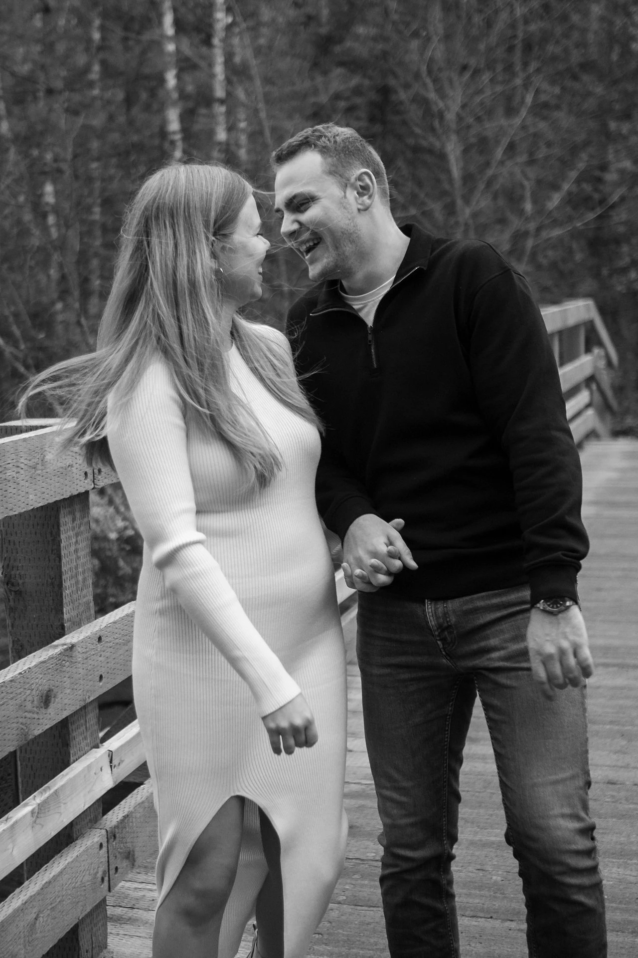A couple laugh on a forest footbridge in a black-and-white photograph