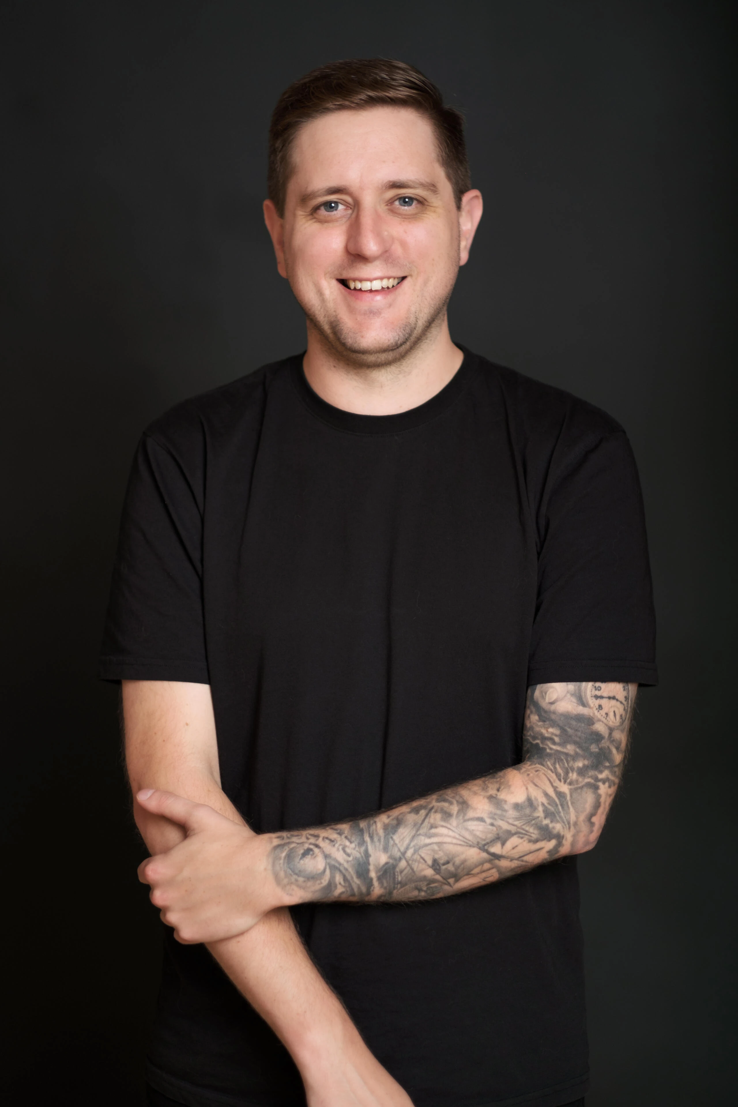 Man in a black shirt smiling against a dark studio background